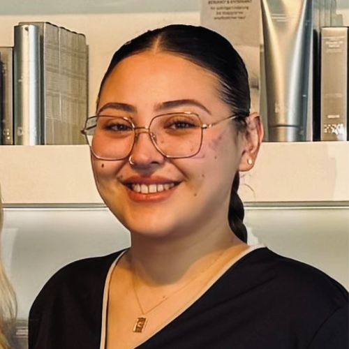 Porträt der Fachkosmetikerin Bircan Seyrek: dunkelhaarige Frau mit Brille, die lächelnd in die Kamera schaut.
